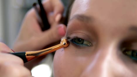 Eyes-make-up-process.-Artist-corrects-eye-line-using-a-professional-brush-with-golden-edge.-Close-up-of-a-model's-face