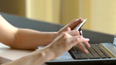 Close-up-woman's-hands-holding-a-credit-card-and-using-computer-keyboard-for-online-shopping