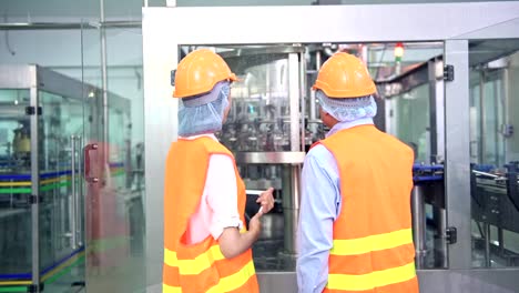 Senior-quality-inspector-teaching-junior-team-member-in-factory.-Chinese-old-male-with-his-young-team-discussing-quality-issue-with-bottle-production-line-in-background.