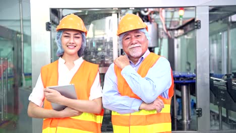 Inspector-de-calidad-superior-docente-a-miembro-del-equipo-junior-en-fábrica.-Varón-de-China-con-su-joven-equipo-de-calidad-tema-con-línea-de-producción-de-la-botella-en-el-fondo.