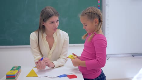 Porträt-von-glücklich-professioneller-Lehrer-weibliche-smart-Schulkind-Mädchen-mit-Kunststoff-Figuren-in-der-hand-in-der-Nähe-von-Board-im-Klassenzimmer-der-Schule