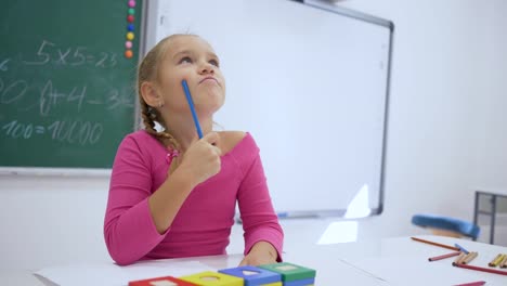 Educación-de-los-niños,-colegiala-escribe-una-tarea-en-el-cuaderno-sentado-en-el-escritorio-en-un-salón-de-clases-sobre-fondo-de-pizarra