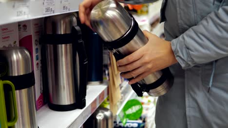 A-young-woman-chooses-a-steel-thermos-in-the-supermarket.