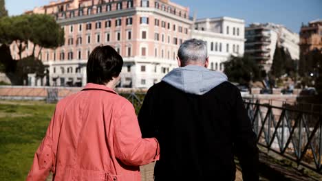 De-nuevo-vista-hermosa-romántica-senior-feliz-pareja-caminando-juntos-sosteniendo-las-manos-de-vacaciones-a-comienzos-de-otoño-Roma,-Italia.