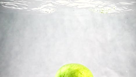 The-green-Apple-falls-into-the-water-at-a-slow-pace.-Fruits-isolated-on-a-white-background.