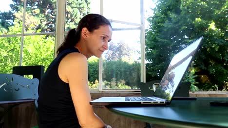 Woman-on-her-laptop-computer-reading-an-article-on-the-internet.-Mother-woking-from-her-balcony-home.