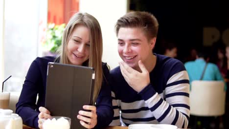 Young-attractive-couple-using-digital-tablet-computer,-looking-at-the-screen-in-cafe.