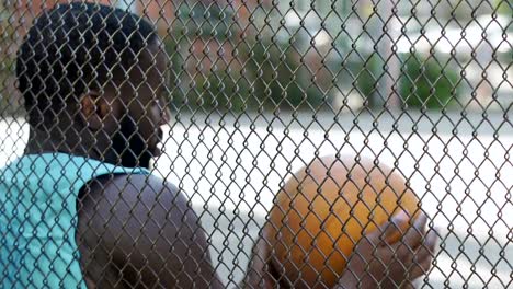 Muscular-male-sitting-near-playground-net-bouncing,-waiting-for-team-players