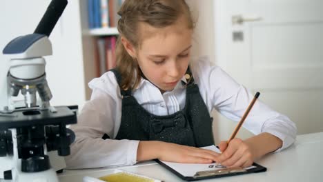 Little-girl-in-science-class-with-microscope-on-the-table.