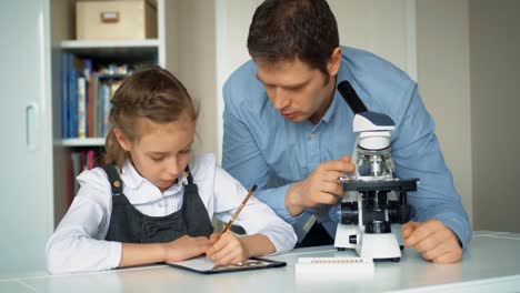 Kleines-Mädchen-mit-Lehrer-im-naturwissenschaftlichen-Unterricht-mit-Mikroskop-auf-dem-Tisch.