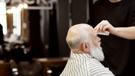 Friseur-schneidet-grauen-Bart-mit-elektrischen-Rasierapparat,-senior-woman