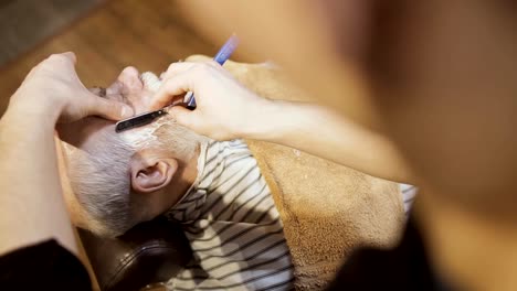 Stylist-makes-modern-beard-to-mature-man-with-sharp-blade