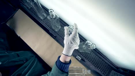 Bottles-go-on-a-conveyor,-while-a-woman-examines-their-quality-on-a-light-background.-4K.