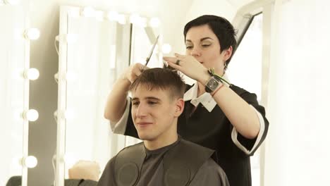 Woman-hairstylist-combing-hair-before-cutting-with-hairdressing-scissors-in-barber-shop.-Haircutter-doing-male-hairstyle-with-comb-and-hairdressing-scissors-in-beauty-studio