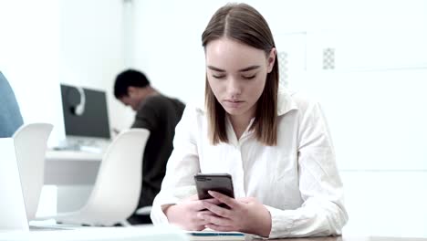 Medium-shot-of-beautiful-female-student-using-her-cell-phone-while-sitting-at-desk-in-computer-class