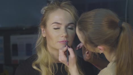 Estilista-de-maquillaje-con-cosméticos-lápiz-para-labios-conforman-en-estudio-de-belleza