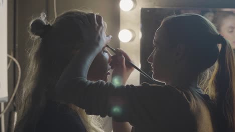 Visagist-Frau-im-Studio-Lidschatten-auf-Augenlid-beim-Make-up-Gesicht-zuweisen