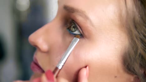 Seitlicher-Blick-auf-einer-Modellfläche.-Make-up-Artist-Lidschatten-unter-dem-unteren-Augenlid-mit-Pinsel-auftragen.-Blauen-Eyeliner.-Prozess-machen