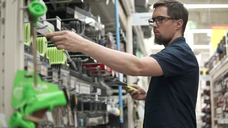 Man-is-holding-two-metal-shovels-in-hands-in-a-department-of-store-for-builders