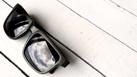 Time-lapse---Blue-skies-reflecting-in-sunglasses-on-wooden-table.-copy-space