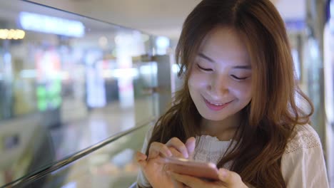 Joven-mujer-de-uso-del-teléfono-móvil-en-el-centro-comercial