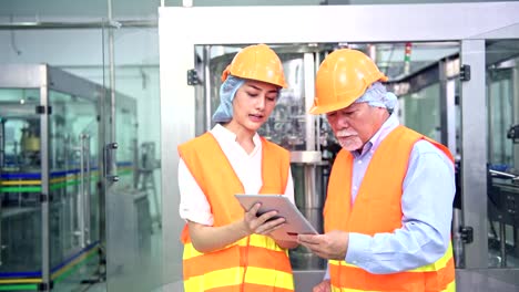 Senior-quality-inspector-teaching-junior-team-member-in-factory.-Chinese-old-male-with-his-young-team-discussing-quality-issue-with-bottle-production-line-in-background.