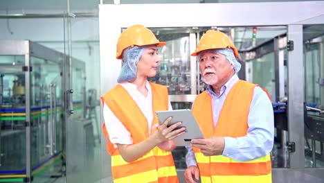 Senior-quality-inspector-teaching-junior-team-member-in-factory.-Chinese-old-male-with-his-young-team-discussing-quality-issue-with-bottle-production-line-in-background.