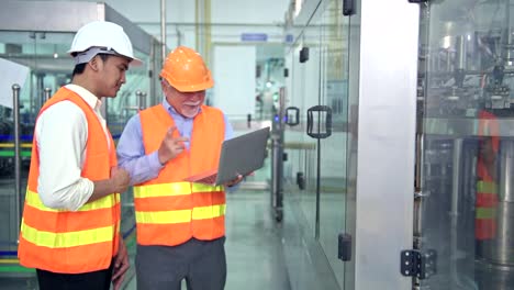 Senior-quality-inspector-teaching-junior-team-member-in-factory.-Chinese-old-male-with-his-young-team-discussing-quality-issue-with-bottle-production-line-in-background.