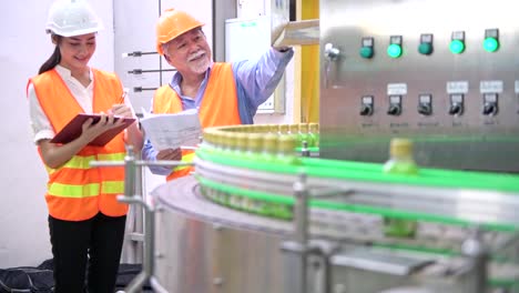 Senior-quality-inspector-teaching-junior-team-member-in-factory.-Chinese-old-male-with-his-young-team-discussing-quality-issue-with-bottle-production-line-in-background.