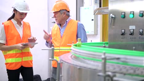 Senior-quality-inspector-teaching-junior-team-member-in-factory.-Chinese-old-male-with-his-young-team-discussing-quality-issue-with-bottle-production-line-in-background.