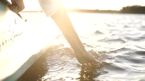 At-sunset,-close-up-the-hand-of-a-girl-moving-through-the-water