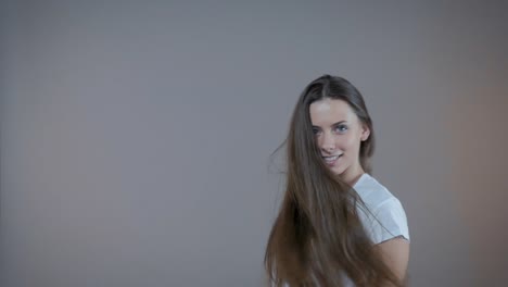 A-young-sports-model-demonstrates-her-long-hair,-I'm-in-the-studio-on-a-gray-background.-Slow-motion