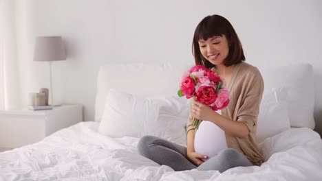 feliz-embarazada-de-Asia-con-flores-en-la-cama