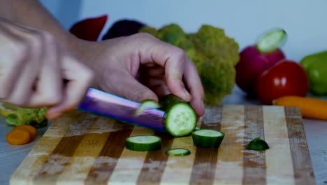 Man-is-cutting-vegetables-in-the-kitchen,-slicing-cucumber-in-slow-motion
