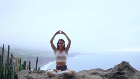 A-woman-sitting-on-top-of-a-mountain-meditates-and-makes-a-gesture-with-her-hands-Maha-Sakal-.-Against-the-ocean-and-green-mountains