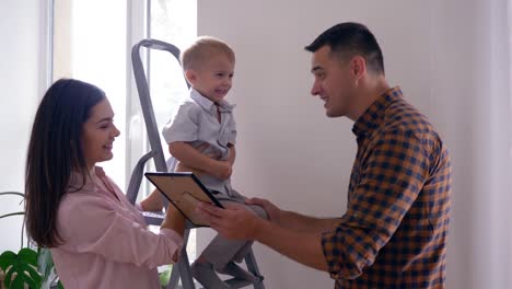 young-family-happy-at-new-apartment-during-interior-decoration,-cheerful-father-plays-with-son-and-wife-kisses-husband