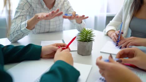 closeup-young-people-hands-with-pens-and-notebooks-on-table