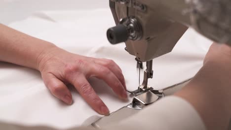 A-closeup-of-a-sewing-machine-stitching-white-fabric.-Female-hands-sewing-it-for-the-wedding-dress