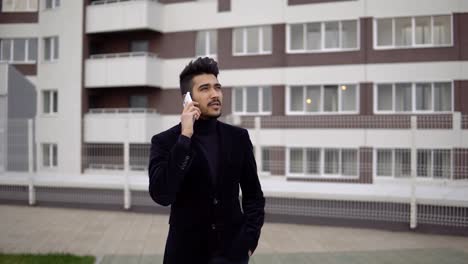 Portrait-of-attractive-slender-businessman-in-formal-suit-talking-on-smartphone-against-the-backdrop-of-business-center