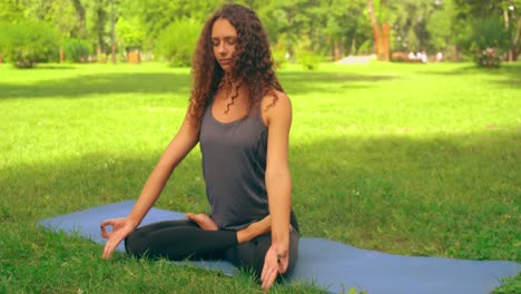 mujer-con-cabello-rizado-meditando-sentada-en-el-césped