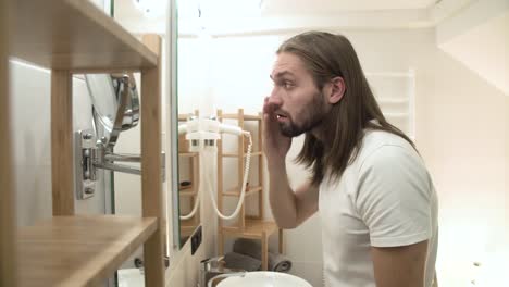 Man-In-Bathroom-Looking-In-Mirror-And-Touching-Face