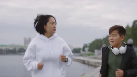 Asiatische-Mutter-und-Sohn-laufen-am-Flussufer-in-der-Stadt-entlang