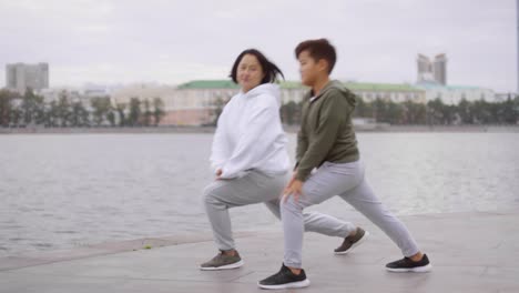 Sportive-Asian-Mother-and-Son-Doing-Lunges-while-Training-on-City-Riverside