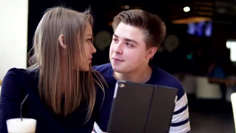 Young-attractive-couple-using-digital-tablet-computer,-looking-at-the-screen-in-cafe.