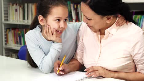 Mujer-asiática-madura-feliz-ayudando-a-su-hijita-con-el-estudio-de