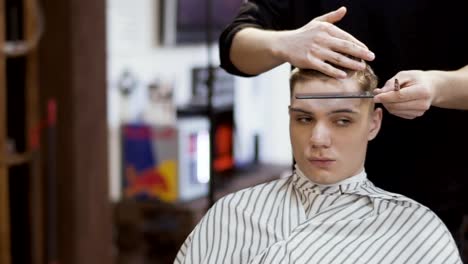 Hairdresser-cuts-hair-of-young-man-in-barbershop