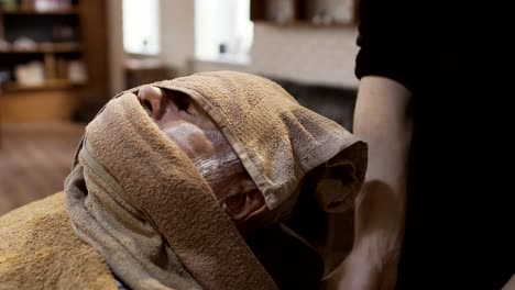 Barber-covers-face-of-senior-man-with-hot-towel-before-shaving