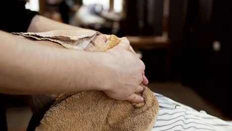 Stylist-covers-face-of-mature-man-with-hot-towel-before-shaving