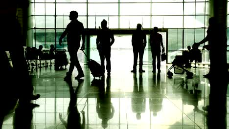 Silhouette-of-passenger-with-suitcase-walking-through-hall-at-airport