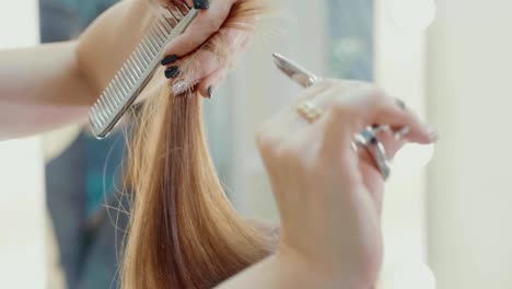 Female-hairdresser-cutting-hair-tips-with-hairdressing-scissors-in-beauty-salon.